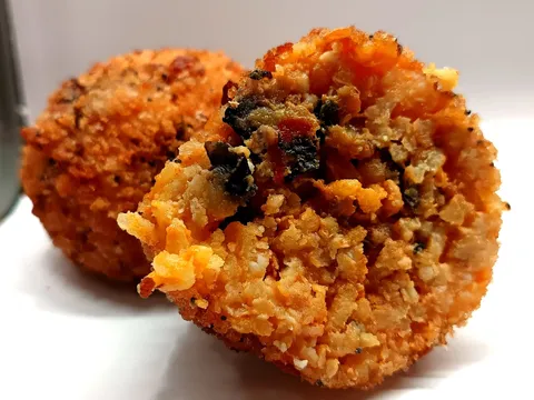 Arancino alla Norma tagliato a metà, ripieno rosso con melanzane e ricotta salata