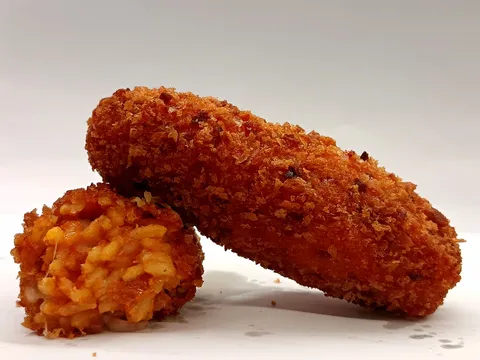 Supplì di riso tagliato a metà, ripieno rosso al pomodoro e carne